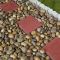 Decorative Royal Tan pebbles used as a natural mulch alternative in a garden bed, providing a warm contrast to green shrubbery